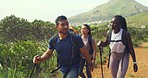 Hikers walking along a trail on a mountain with hiking sticks. Diverse group of young active and adventurous friends exploring a rugged path in nature. Happy tourists enjoying a scenic trek outdoors
