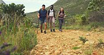A diverse group of active mountain hikers walking on a lush green trekking trail. Friend clique bonding on a social hike in a remote area with plants and bushes. Man and women backpacking in nature