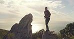 Young mountain hiker admiring scenic view from peak along green hill trekking trail. Woman holding binoculars during rocky hike in remote area with plants and bushes. Fit woman backpacking in nature