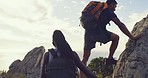 Fit and active hikers helping each other hike up a boulder on a mountain. Young man giving a helping hand to his female friend on a big rock in nature with a cloudy blue sky in the background