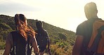 Rearview of hikers walking down a mountain trail with hiking sticks in the sun. Group of active and adventurous friends exploring a path along the coast. Tourists enjoying a scenic trek outdoors