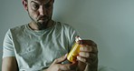 Mentally ill man holding pills in an asylum and thinking. Anxious, unsure man suffering from mental health disorders, depression, bipolar, suicidal thoughts. Curious and rejecting medication drugs 