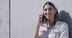 Young woman laughing while talking on the phone with a relative in the city. Female looking cheerful while having a conversation with a friend in town. Girl chatting with a loved one downtown