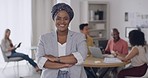 A portrait of an African businesswoman wearing a head scarf standing in the office with folded hands. A female smiling at the camera while her colleagues working in the background.  