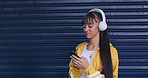 Beautiful young woman using her phone to send a text message with wireless headphones around her neck against a dark background. Using wireless technology to surf the internet or browse social media