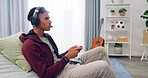 A young gamer talking on a wireless headset while sitting on a couch and playing a console video game. Using a controller to play multiplayer online and having fun while looking serious and focused