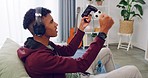 An excited gamer is sitting on a couch, playing a video game on a console. He Plays with a Wired controller. A young boy wearing a headphone wins while playing on a PlayStation.