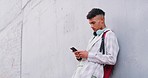 Trendy guy with headphones using his phone outside. Young male student in the millennial age happy to be connected while on the go, listening to music playing online games and texting on social media