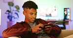 A happy gamer playing on a phone, smiling while relaxing on a sofa. An african american guy streaming video games from a mobile device. A cheerful guy scrolling through a social media app online