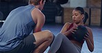 Active woman doing russian twists with a weighted ball while exercising with the help of a fitness coach in a gym. Young athlete breathing while maintaining her balance during a core and abs workout