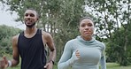 Two fit people running in a park, enjoying their daily exercise and fitness routine outdoors. Confident smiling female jogging and happy african male working out in a quiet scenic location