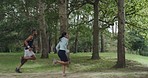 Active people jogging outdoors in a green forest on summer day. Athletic man and woman running together in nature as part of fitness and cardio training. Runners doing their morning workout routine