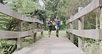 Fit couple running and jogging across a bridge in a park on a sunny day. Motivated and happy young man and woman enjoying a cardio workout together. Exercising in nature to stay healthy and fit

