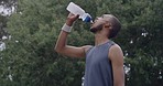 Fit young man drinking water and wiping his sweat after an intense workout outdoors. One tired athlete from below quenching his thirst and cooling down after a challenging and refreshing run 