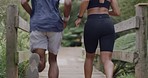 Rear view of two fit athletes running on a bridge in a park on a summer's day. Young healthy couple training together in a park, focused on speed and energy while getting a cardio workout in nature