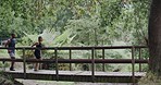 Two athletes running across a footbridge at a park. Sporty young male and female out for a cardio workout. Fitness couple having a race outdoors to make exercising together fun and challenging