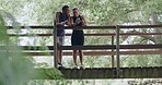 Active couple resting on a bridge after exercising together outdoors in nature. Fit athletes taking a break and using a phone in a park after a cardio workout. Fitness people talking and laughing