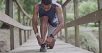 Male athlete tying his laces while on a bridge in a park. Young man making sure his running shoes is fastened. The proper footwear will give you the traction and support you need for your workout