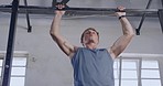 Sporty young man exercising on a chin up bar during his workout at the gym. Dedicated sportsman doing pull ups for stronger arm and back muscles in a fitness facility. The goal is to build muscle