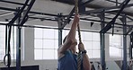 Fit man climbing rope for training exercise in a gym. Strong, active, athletic trainer using upper body strength and strong arms to pull himself up in a HIIT fitness workout. Focused on muscle health