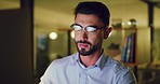 Young business man working late on a computer in an office at night. Face of a hardworking entrepreneur reading emails, doing research online and compiling reports while planning ideas for deadlines