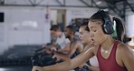 Sweaty female athlete drinking water and taking break inside during an indoor cycling class at gym. Tired and thirsty woman wearing headphones and hydrating during  group cardio at a fitness facility