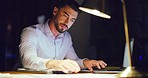 Young business man brainstorming and planning his schedule in a diary with a laptop while working late in an office alone. One serious male professional reading documents and writing in a book