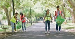 Young volunteers picking up trash together in park. Group of people carrying bags to collect garbage in a botanical garden outside. Diverse garbage collectors doing a routine cleanup at playground  