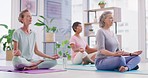 Mature women meditating in lotus pose with mudra hand gesture during a fitness class in a yoga studio. Calm, relaxed and focused ladies sitting and praying quietly for inner peace and zen energy
