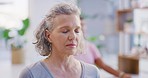 Mature woman meditating with eyes closed during a group fitness class in a yoga studio. Face of a calm, relaxed and focused senior lady sitting and praying quietly for inner peace and zen energy