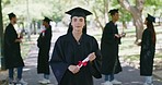 Portrait of a university student at her graduation ceremony outdoors. Woman holding a diploma while celebrating her accomplishment and achievement. Getting a good education for a successful future