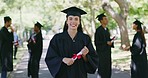 Portrait of a female university or college graduate standing outside with her degree or diploma on graduation day. Young woman in mortarboard and gown celebrating success in education and studies