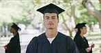 Portrait of a male university or college graduate standing outside an looking at the camera on graduation day. Proud young man in mortarboard and gown celebrating success in education and studies