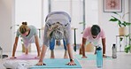 Active mature women bending in a downward facing dog pose during a fitness class in a yoga studio. Yogi training a group of calm and relaxed ladies. Exercising to improve health and wellbeing