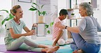 Mature women stretching after yoga class in a modern wellness center on sunny day.  Flexible hip older ladies chatting together on exercise mats and hydrating before meditation and breathing session