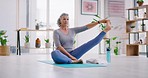 Senior woman doing yoga on a mat in her living room at home. Active woman doing pilates, stretching her legs in a sitting position while practicing balance and meditation for a healthy lifestyle