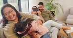 Adorable little girl playing with grandmother, laughing in home living room. Multi generation family enjoying quality time together. Smiling child being tickled while parents use a phone for selfies