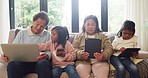 Young adopted sisters and their grandparents using a laptop, phone and tablets while relaxing on a sofa together at home. Adoptive parents and their foster daughters sitting in the living room