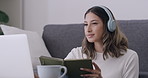 Student taking online course classes at home writing down notes in her note book while wearing wireless headphones.
Smart woman studying while doing research on her education options via her laptop