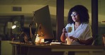 Businesswoman drinking coffee while working late to stay awake while reading reports on a computer in an office at night. Hardworking entrepreneur doing online research for deadline during overtime
