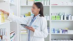 A young female pharmacist stocktaking in a dispensary using a tablet. Doctor preparing prescriptions and medication at clinic or pharmacy. Healthcare professional sorting medicine with digital device