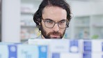 Man with glasses choosing medication on a shelf in a pharmacy. Customer with glasses browsing in aisle in a drugstore and finding what he needs before heading to the checkout with his vitamins