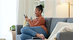 Young lady laughing at phone casually. Relaxed woman sitting on couch in living room wearing everyday clothes. Holding mobile she is smiling and joyful to use modern technology for fun