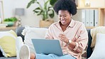 Woman enjoying music on a laptop and listening to songs on wireless earbuds, sitting on the sofa inside at home. Trendy african female with afro dancing and singing along while relaxing on the couch