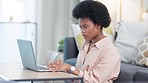 Focused African American female freelancer sits at table at home typing on laptop. Journalist and editor proofreading an article. Concentrating intensely to finish a deadline while working from home.