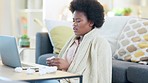 Sick woman using a laptop while working from home. African freelancer with afro suffering from covid or flu and blowing her nose while working remotely or doing online consultation with her doctor