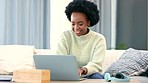 Afro woman typing on laptop and learning how to trade on the stock market with distance learning course. Smiling, happy and relaxed woman sitting alone in home living room and searching on technology