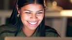 A happy business woman working overtime in the evening inside a restaurant. The face of a dedicated female entrepreneur smiling and typing on a laptop at night. A committed corporate professional