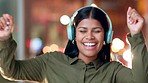 Happy woman wearing headphones and dancing while working late at night in a modern office with background of bokeh and blurry lights. Excited female with lots of energy celebrating good news at work