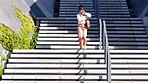 Business woman running down the stairs leaving work in a rush on a phone call in the city. Black female corporate professional running in an emergency while having a conversation with a loved one